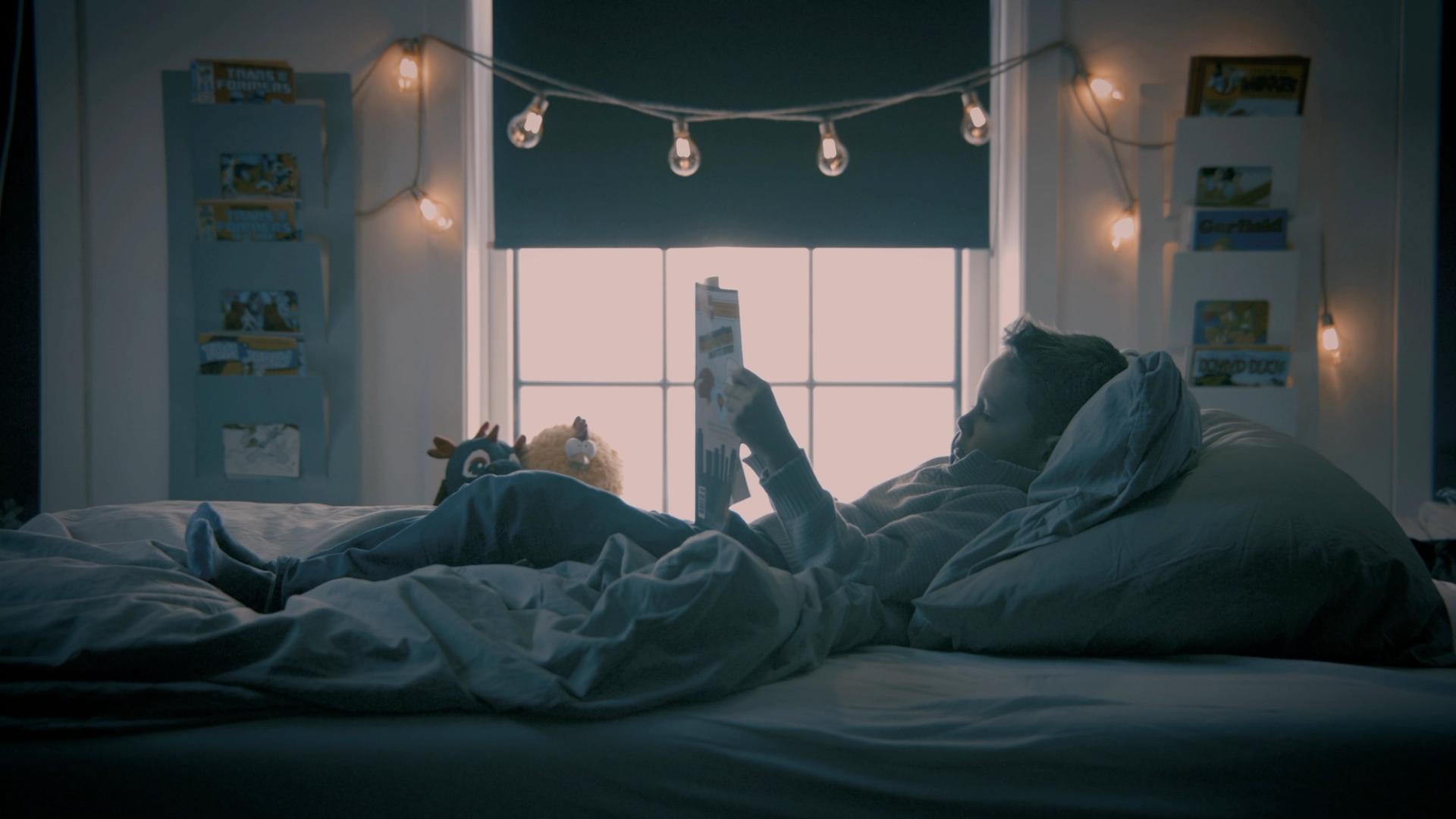 En gutt ligger i sengen og leser et blad 