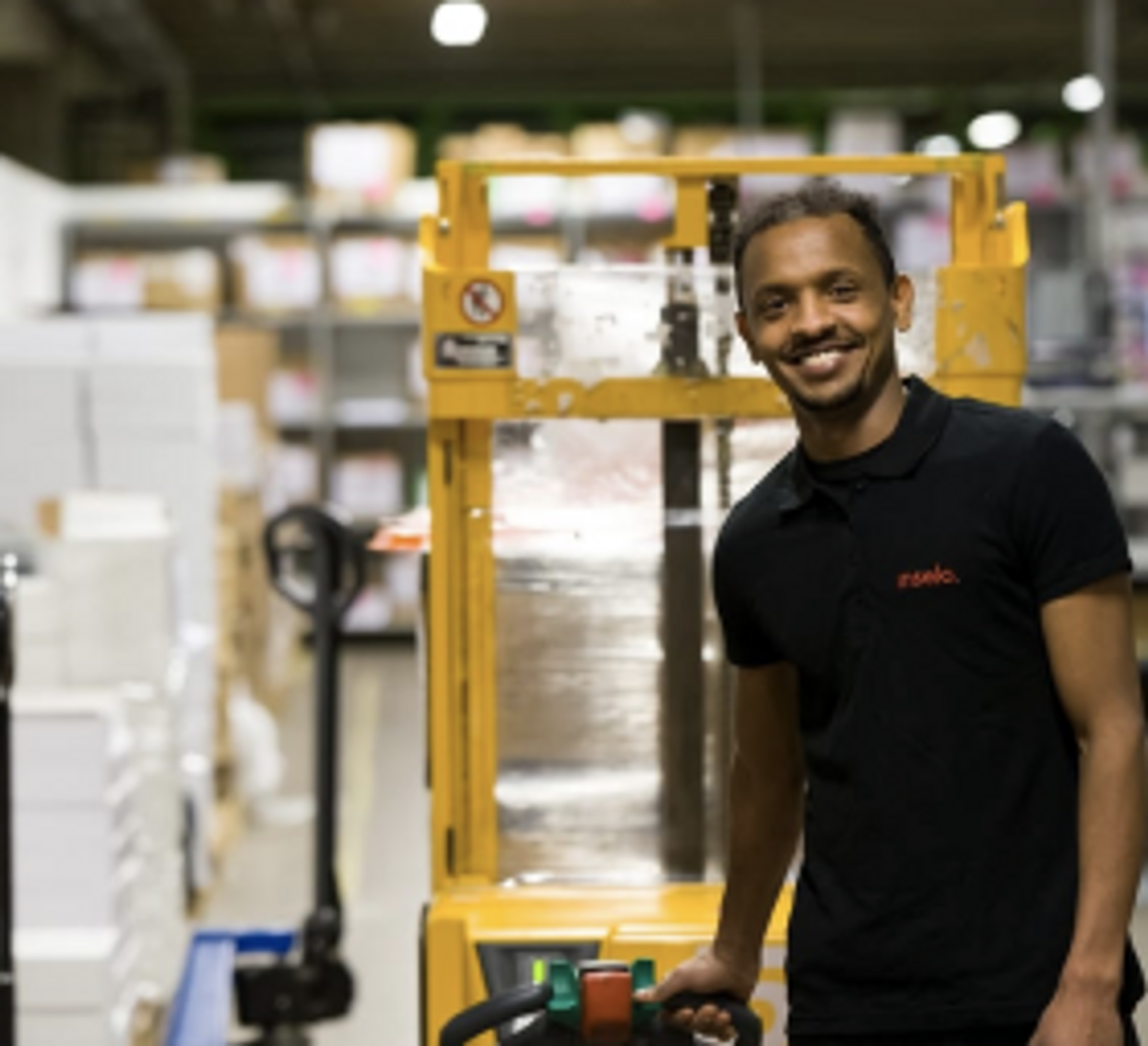 Kundereisehelt på logistikk smiler lent mot en gaffeltruck 